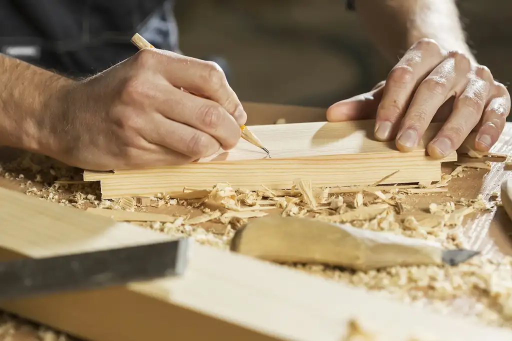 Close-up of hands marking a wooden board with a pencil