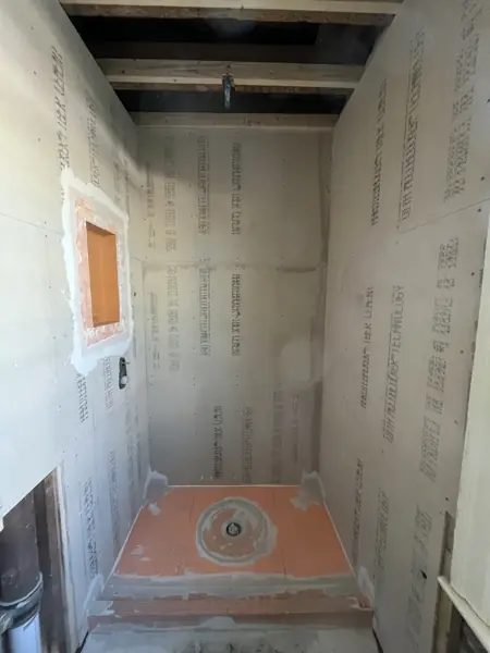 New shower stall with cement backer board on the walls, an orange shower pan with a center drain, and a recessed niche framed in.